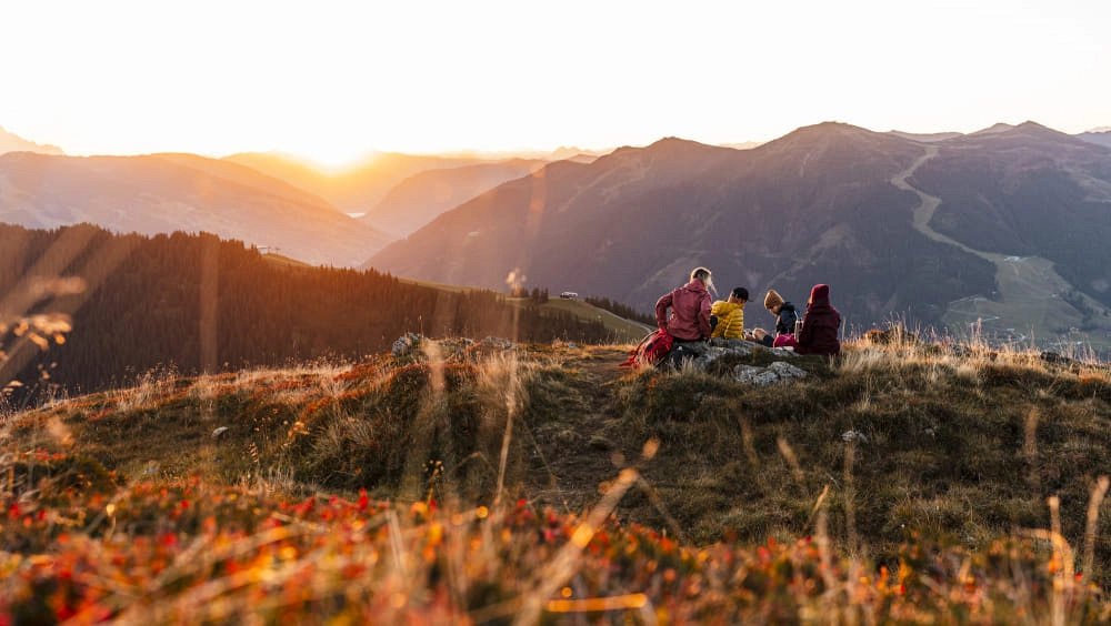 Drei Wanderer sitzen auf einem Hügel in Saalbach Hinterglemm im Herbst.